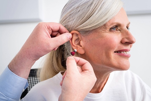 Ältere Frau bekommt ein modernes Hörgerät eingesetzt, Hörhilfe und Hörakustik-Beratung.